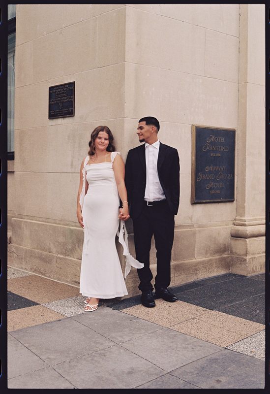 Juan David and Hannah holding hands beside the bronze plaque of a stone building