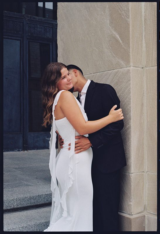 Hannah resting her head against Juan David's as they embrace beside a stone wall