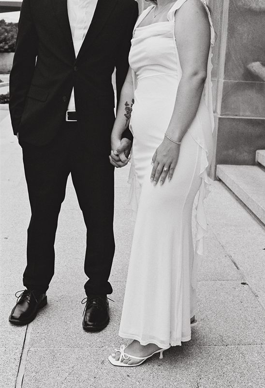 Juan David and Hannah holding hands, seen from the shoulders down, in black and white