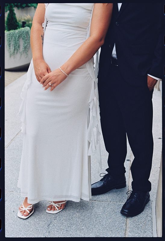 Hannah's hands clasped in front of her white dress, Juan David beside her